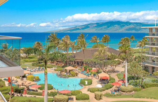 A resort with a swimming pool, palm trees, and a view of the ocean.