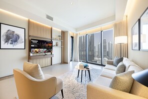 A modern hotel room with a sofa, armchairs, a small coffee table, a TV, and a city view. - NEW | 3BR Burj Fountain NYE View | Address (Dubai)