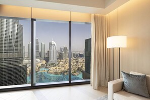 A modern hotel room with a large panoramic window, a sofa, a lamp, and a view of a cityscape.