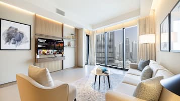 A modern hotel room with a sofa set, a small coffee table, and a bar area with a TV.
