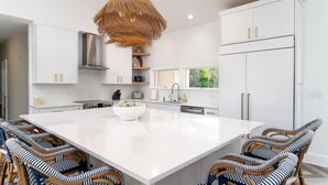 A modern kitchen with white cabinetry, a large island, wicker chairs, and a hanging light fixture. - Fabulous Location! Sleeps 12! Walk to Club/Beach! Amenity access included (Seabrook Island)