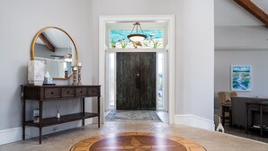 A foyer with a large mirror, a console table, a wooden floor with a geometric pattern, a dark wooden door, and a stained glass window above the door. - Fabulous Location! Sleeps 12! Walk to Club/Beach! Amenity access included (Seabrook Island)