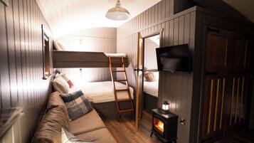A cozy room with a bunk bed, a sofa, a television, and a wood-burning stove.