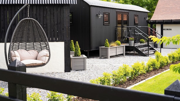 A modern building with a black exterior, a hanging chair, and a well-maintained garden area. - Charming Lodge in Limavady, Sleeps 5 with Parking (Limavady)