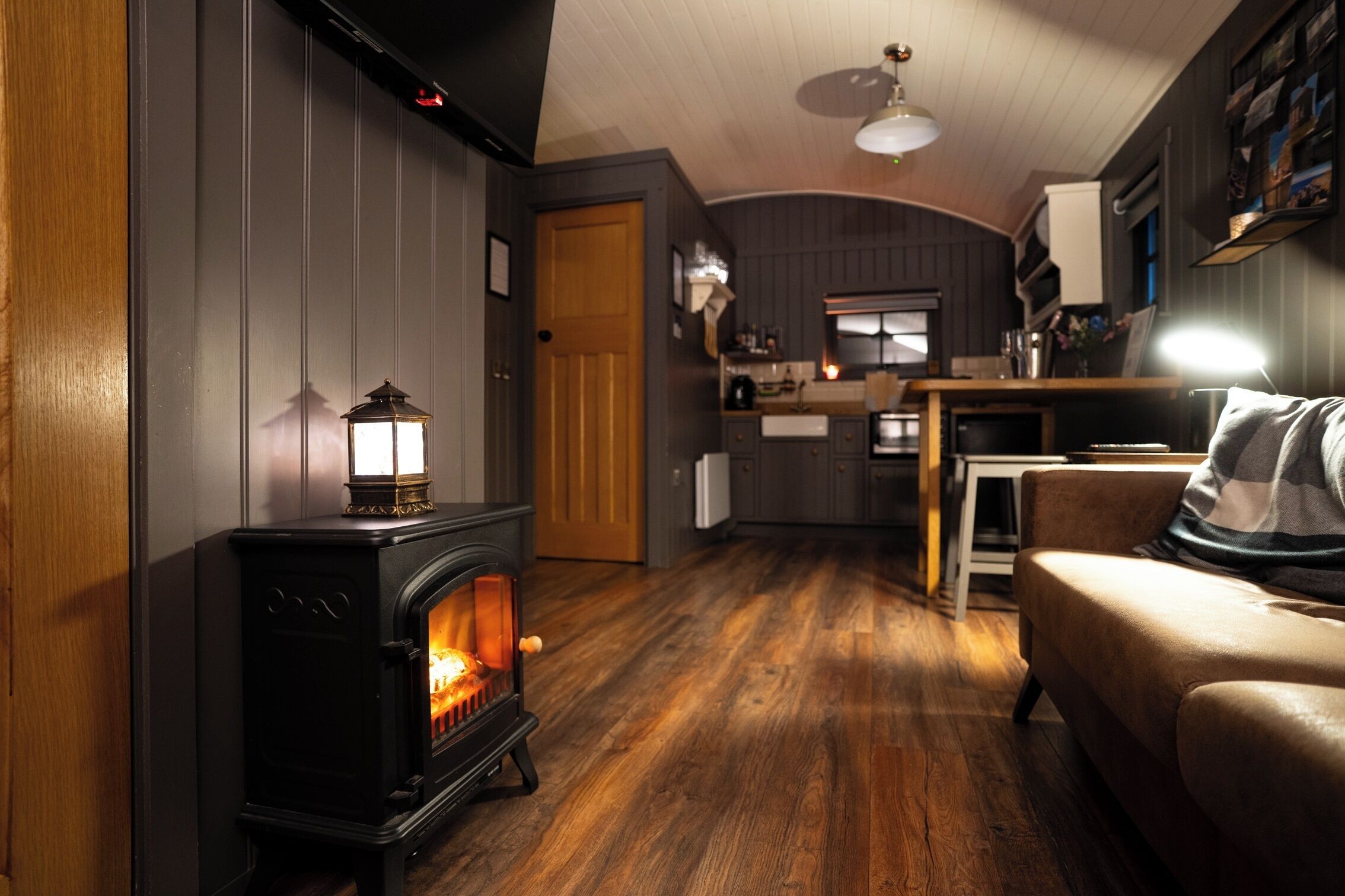 A cozy living room with a wood-burning stove, a sofa, and a dining area with a kitchen in the background.