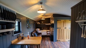 A compact kitchen with a wooden table, bar stools, and a bunk bed in the background. - Charming Lodge in Limavady, Sleeps 5 with Parking (Limavady)