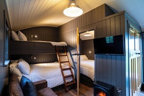 Un dormitorio pequeño con literas, una escalera de madera, un televisor y una chimenea.