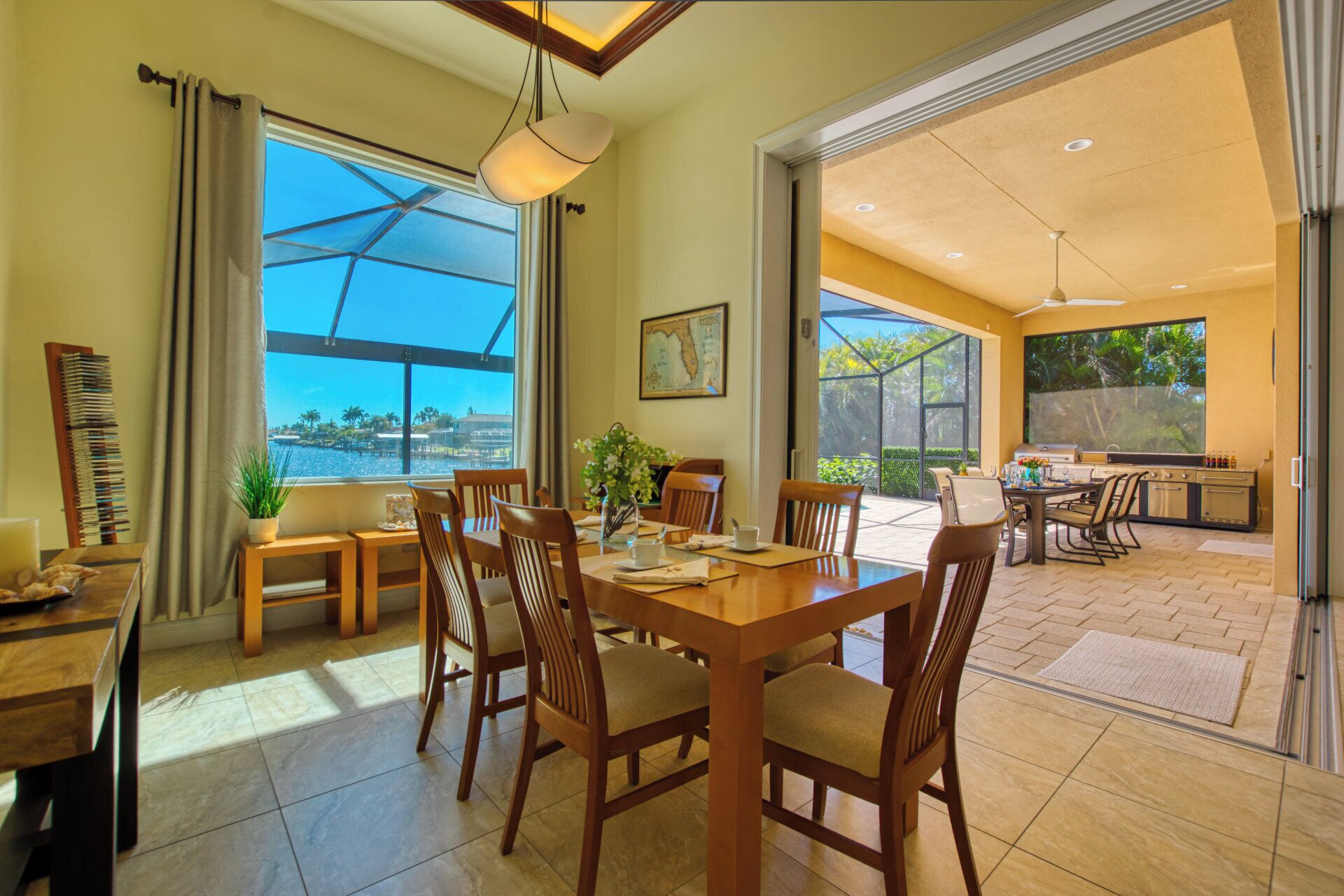 A dining area with a large table, chairs, and a view of the ocean. There is a kitchen area with a grill and a dining table with chairs.