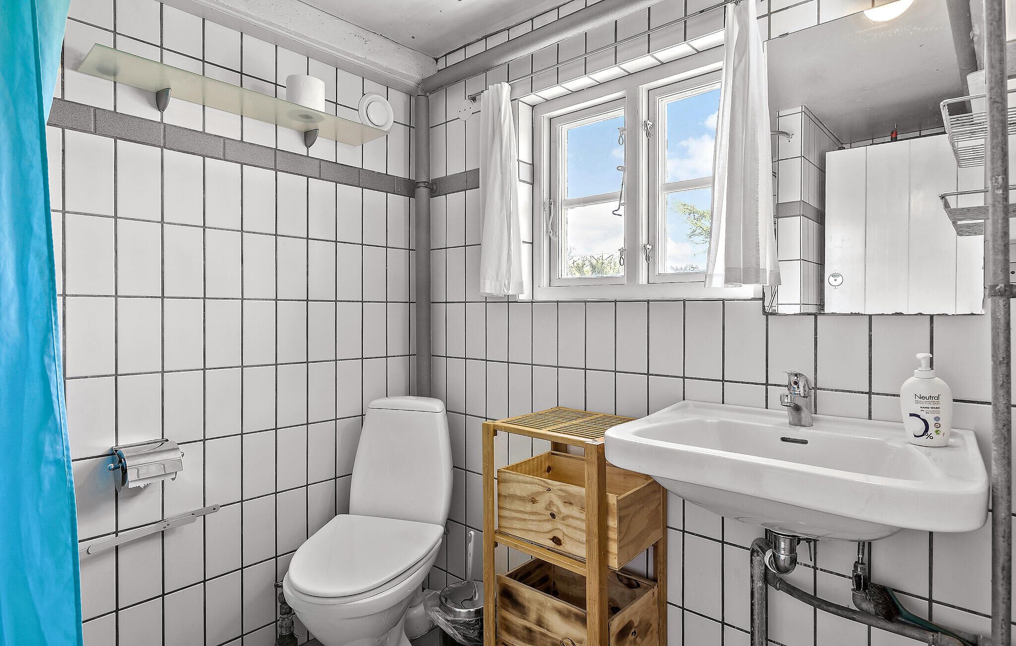 A bathroom with a toilet, a wooden shelf, a sink, and a window.