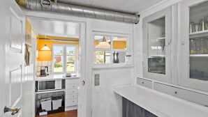 Une cuisine étroite avec des meubles blancs, une fenêtre donnant sur un mur jaune et des conduits apparents au plafond.
