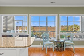 A kitchen with a granite countertop, two light blue chairs, a small round table, and a view of the landscape through large windows.