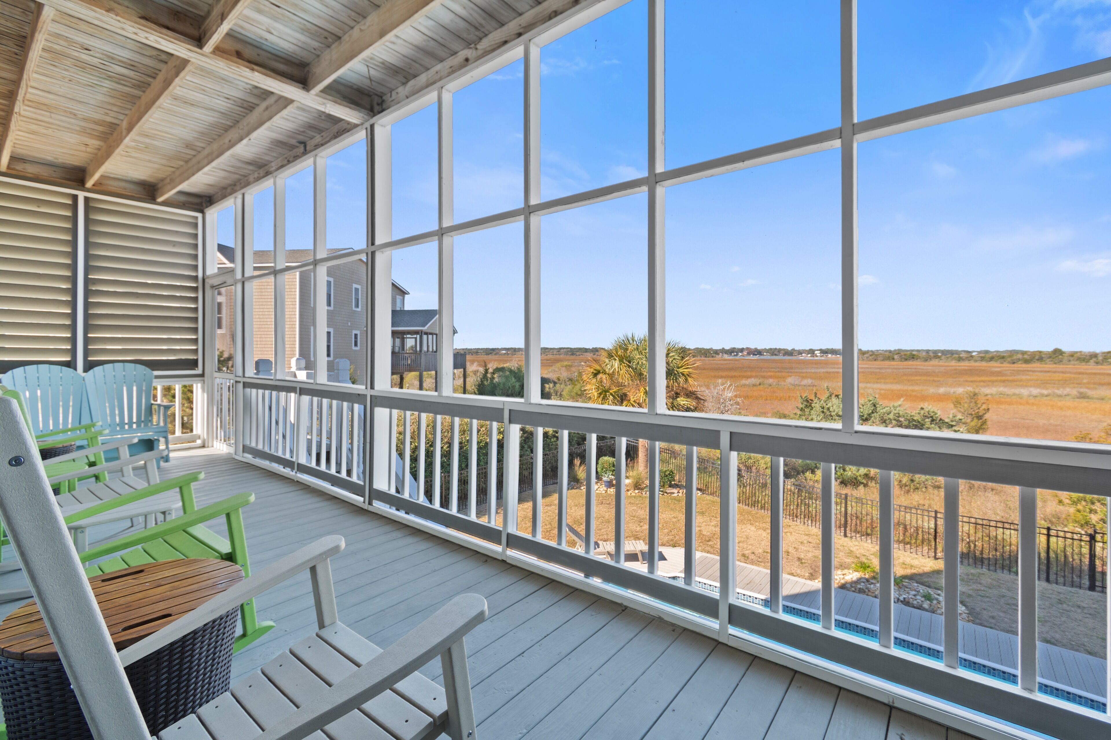 A covered porch with white railings and green chairs, overlooking a rural landscape.