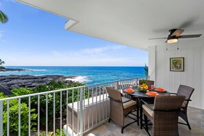 Un balcon avec une table dressée pour le dîner, offrant une vue sur la côte, l’océan et un rivage rocheux.