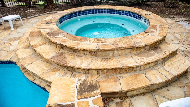 Un jacuzzi circulaire, dont l’intérieur est revêtu de carreaux, entouré d’escaliers en pierre et d’une piscine.
