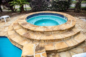 Una bañera de hidromasaje circular con interior de azulejos, rodeada de escalones de piedra y una piscina.
