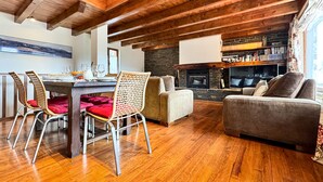 Un salon chaleureux avec une cheminée, un coin repas avec une table dressée pour quatre personnes et un canapé confortable.