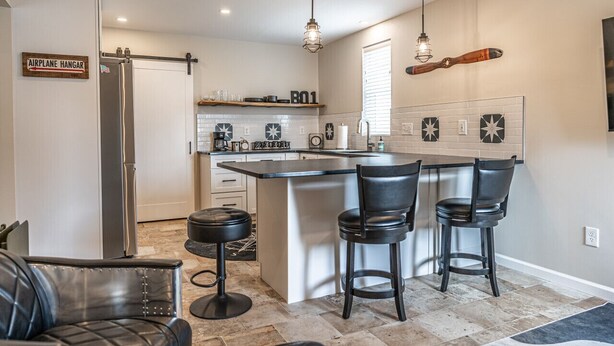 A modern kitchen with a central island, bar stools, and pendant lighting. - ✈️ Full Stop Landing | Aviation Retreat Near Pinehurst (Carthage)