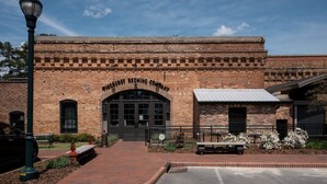 A brick building with a large arched entrance, a small attached structure with a metal roof, and a paved walkway leading to the entrance. - ✈️ Full Stop Landing | Aviation Retreat Near Pinehurst (Carthage)
