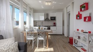Une cuisine moderne avec des meubles blancs, une table à manger en bois et une poubelle rouge.