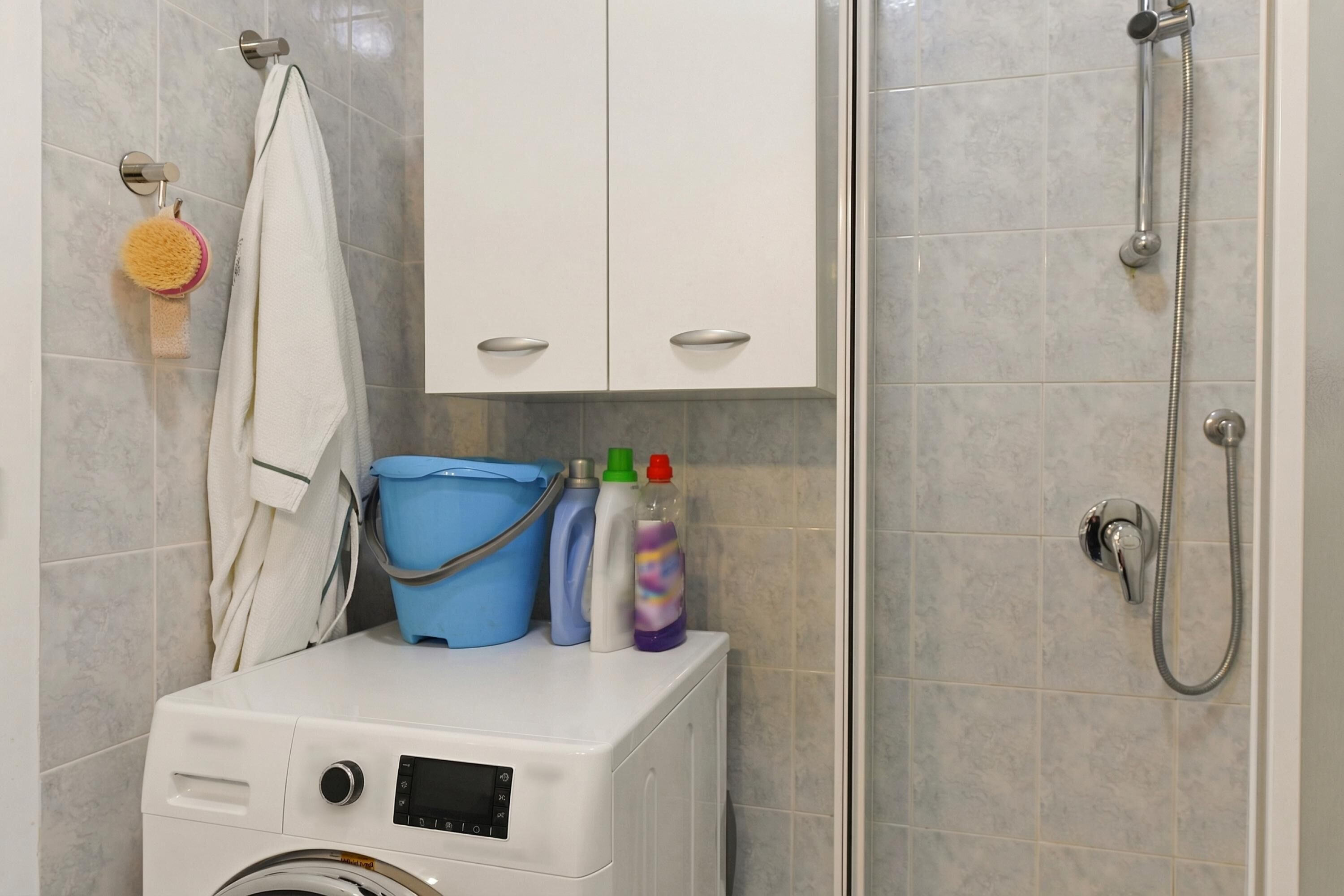 Ein Badezimmer mit Waschmaschine, Dusche und Ablage für Toilettenartikel.