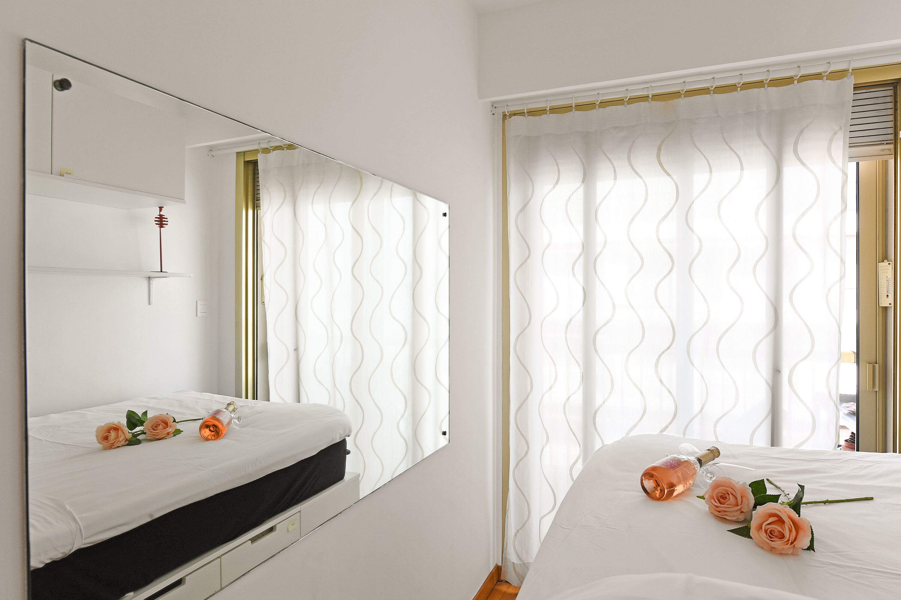 A hotel room with two beds, a large mirror, and a window with a wavy curtain.