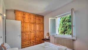 A bedroom with a bed, a wooden wardrobe, a window with a view of greenery, and a radiator. - Casa al Cor - Star in Torbole, Torbole sul Garda, Italy (Torbole sul Garda)