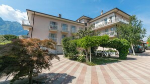 A multi-story hotel with balconies, a paved courtyard, and a mountain backdrop. - Casa al Cor - Star in Torbole, Torbole sul Garda, Italy (Torbole sul Garda)