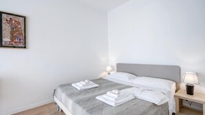 Una cama bien hecha con sábanas y toallas blancas, una mesita de noche con lámpara y una obra de arte enmarcada en la pared.