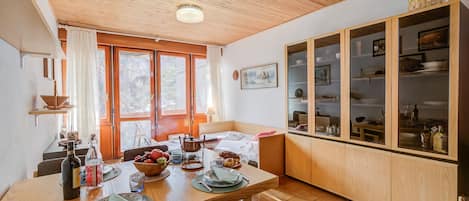 A dining area with a wooden table set for two, a kitchen with wooden cabinets, and a large window with curtains.