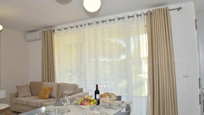 A dining area with a table set for two, a sofa, and a window with curtains.