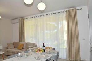 A dining area with a table set for two, a sofa, and a window with curtains.