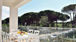 A balcony with a table set for breakfast, overlooking a road with parked cars and trees in the background.