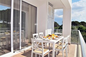 Een balkon met een eettafel voor vier personen, witte stoelen en een fruitmand.