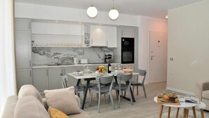A modern kitchen with white cabinets, a marble backsplash, and a dining area with a table and chairs.