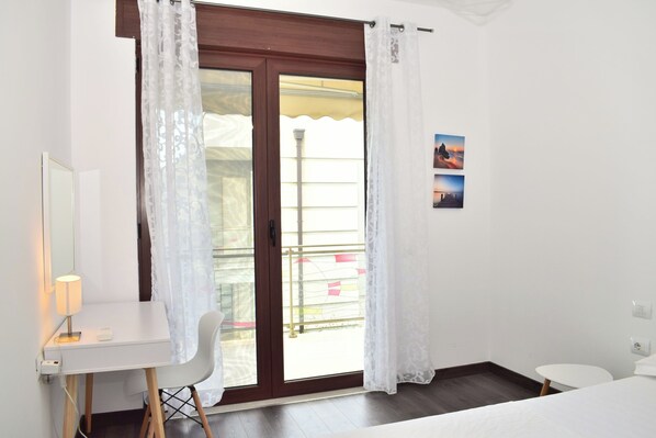 A room with a desk, chair, bed, and a sliding glass door to an outdoor balcony.