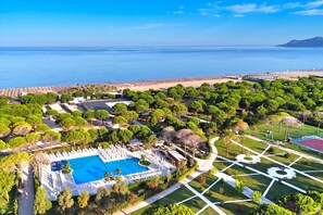 An aerial view of a resort with a swimming pool, landscaped gardens, and a beach.