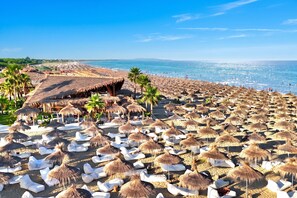 A beach with numerous thatched umbrellas and white lounge chairs.