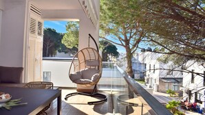 Un balcón con una mesa de comedor, una silla colgante y barandilla de vidrio con vistas a una zona residencial.