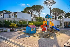 A playground with a slide and climbing structures, surrounded by a paved area and trees. - San Pietro Serenity Home, Lalzit Bay, Albania (Lalzit Bay)