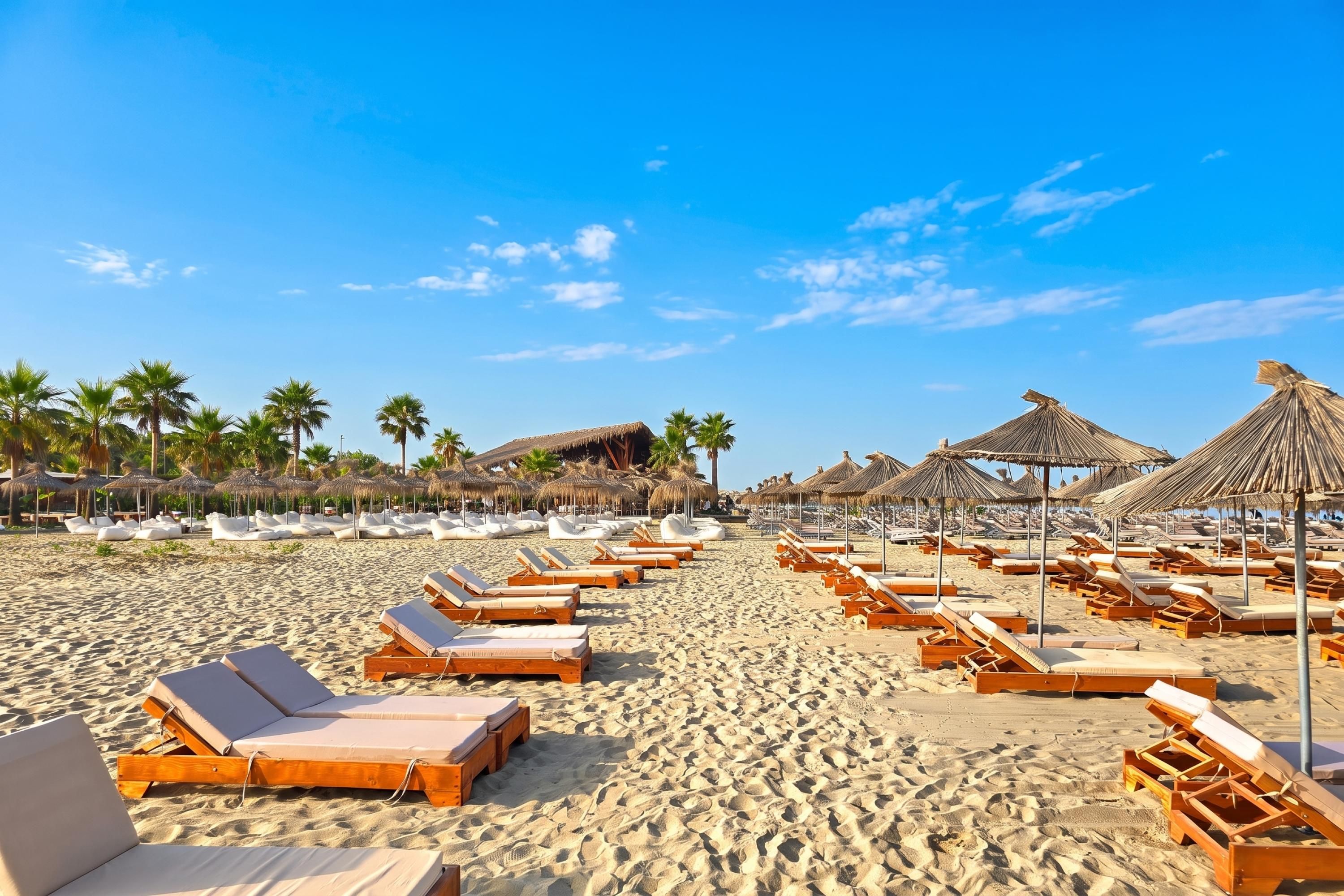 Une plage bordée de rangées de chaises longues et d’ombrelles en chaume.