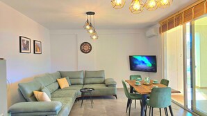 Un saló modern amb un sofà modular, una taula de dinar amb cadires, una televisió de pantalla plana i il·luminació penjant.
