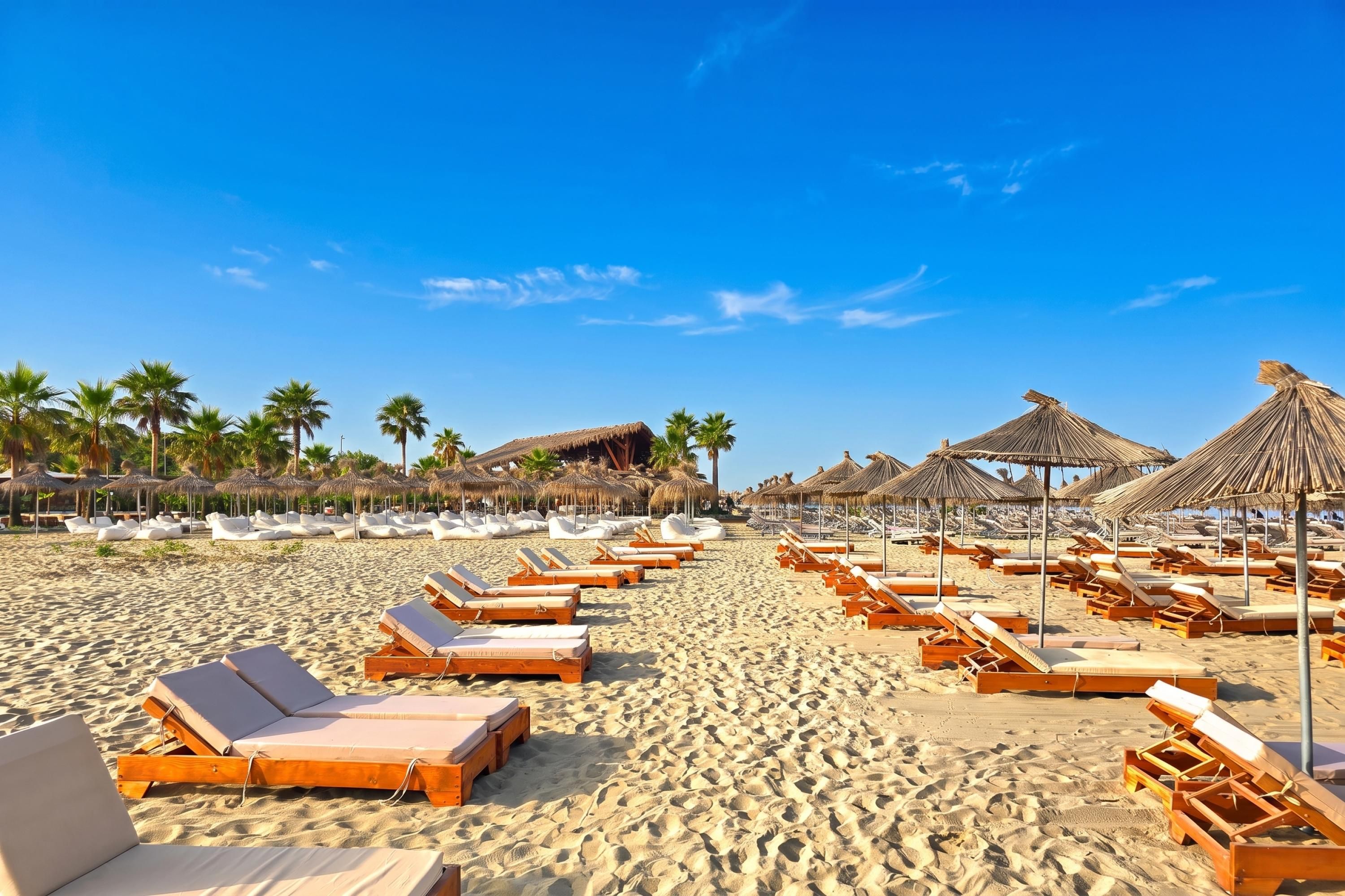 Une plage bordée de rangées de chaises longues en bois et d’ombrelles en chaume.