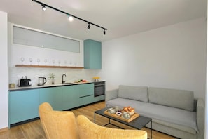 Een moderne keuken met blauwgroene kastjes, een grijze bank en een salontafel met een schaal gebak.