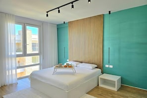 Un dormitorio moderno con una cama, una bandeja con alimentos para el desayuno, una mesita de noche y vistas a través de un amplio ventanal.