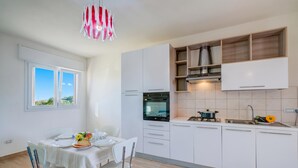 A modern kitchen with white cabinets, a built-in oven, and a dining area with a table and chairs. - Le Bianche Apt1 with Garden Near The Sea, Manduria, Italy (Manduria)