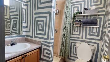 A bathroom with a geometric patterned wall, a sink with a mirror, wooden cabinets, a toilet, and a shower area.