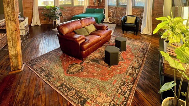 A spacious living room with a leather sofa, a large rug, and a ceiling fan. - 420 Loft Canada Bridge View - FREE PARKING - FREE WIFI (Detroit)