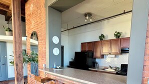 A kitchen with a brick wall, wooden bar stools, a black refrigerator, and wooden cabinets. - 420 Loft Canada Bridge View - FREE PARKING - FREE WIFI (Detroit)