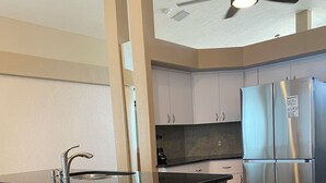 A modern kitchen with a central island, bar stools, a stainless steel refrigerator, and a ceiling fan.