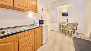 A modern kitchen with wooden cabinets, a microwave, and a sink. There is a dining area with a table and chairs, and a television mounted on the wall. - Villa Belvedere by Interhome (Janské Lázně)